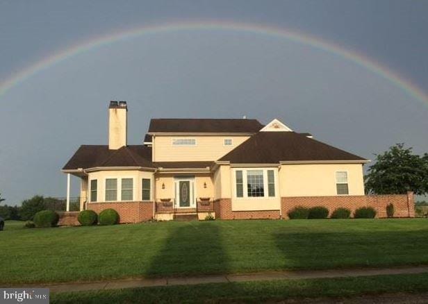 view of front of home featuring a chimney, a front lawn, and brick siding