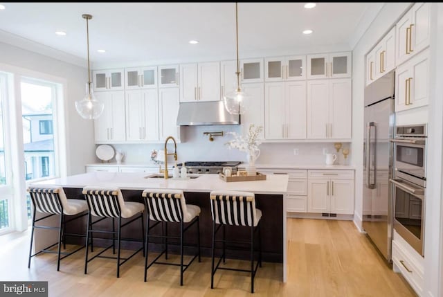 kitchen with under cabinet range hood, white cabinetry, light countertops, and a sink