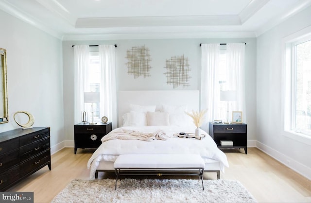 bedroom featuring ornamental molding, light wood-type flooring, a raised ceiling, and baseboards