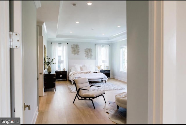 bedroom featuring light wood-style floors, multiple windows, and a tray ceiling