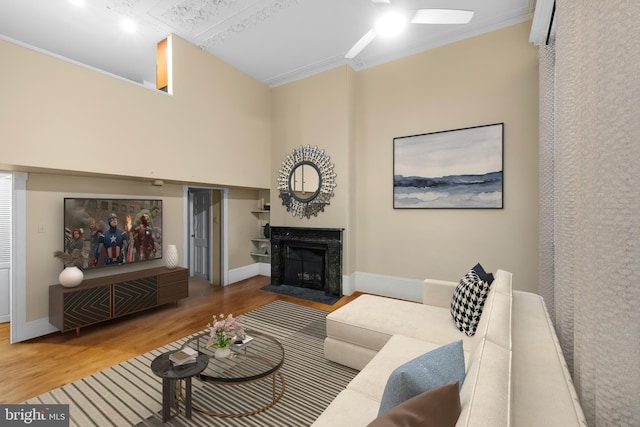 living room featuring a fireplace with flush hearth, baseboards, wood finished floors, and crown molding