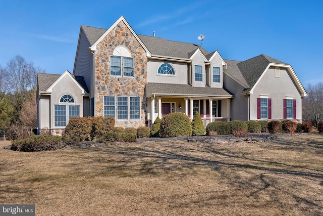 traditional home with stone siding, a front lawn, covered porch, and stucco siding