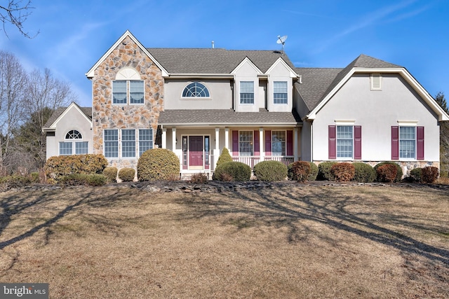 traditional home featuring stone siding, a shingled roof, covered porch, and stucco siding