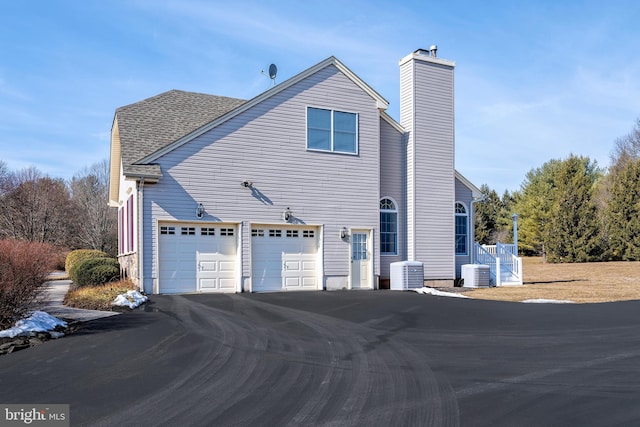 view of home's exterior with a garage, aphalt driveway, roof with shingles, and central air condition unit