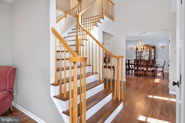 stairs with a chandelier, a high ceiling, wood-type flooring, and baseboards