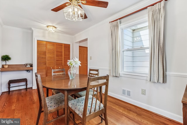 dining room featuring a ceiling fan, wood finished floors, visible vents, baseboards, and crown molding