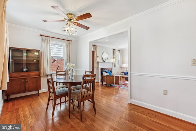 dining area with a fireplace, crown molding, baseboards, and wood finished floors