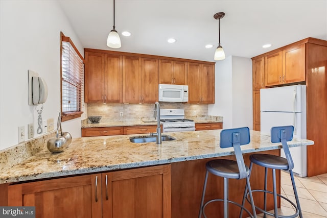 kitchen with white appliances, light tile patterned floors, brown cabinetry, light stone countertops, and a sink