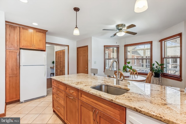 kitchen featuring brown cabinets, a sink, white appliances, light tile patterned flooring, and hanging light fixtures