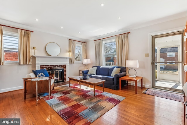 living area featuring hardwood / wood-style floors, baseboards, recessed lighting, ornamental molding, and a brick fireplace