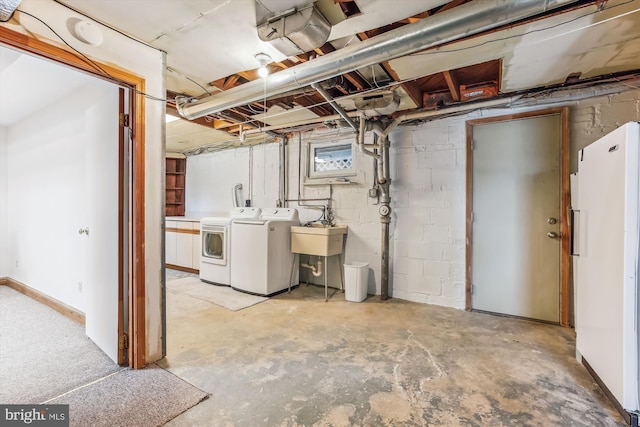 unfinished basement featuring concrete block wall, washing machine and dryer, freestanding refrigerator, and a sink