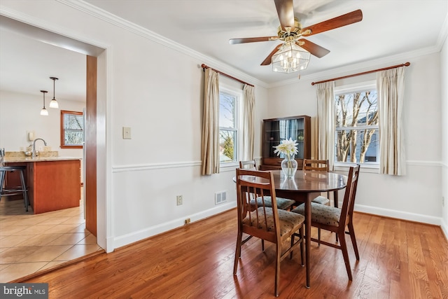 dining area featuring light wood finished floors, a ceiling fan, baseboards, and ornamental molding