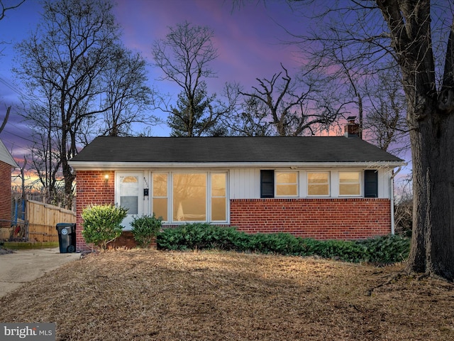 view of front facade featuring a chimney, fence, and brick siding