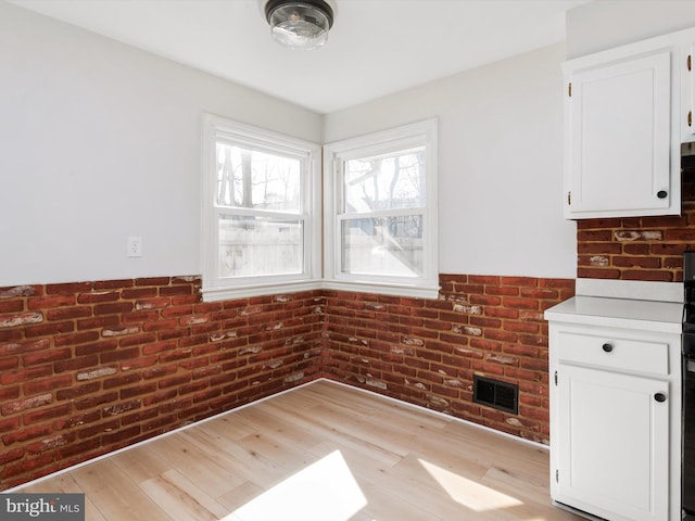 unfurnished dining area with light wood-type flooring, a wainscoted wall, brick wall, and visible vents