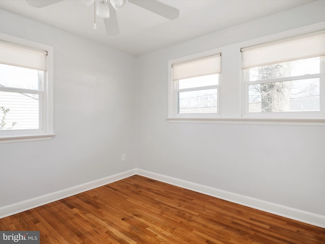 empty room with a healthy amount of sunlight, a ceiling fan, baseboards, and wood finished floors