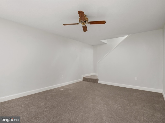 spare room featuring ceiling fan, dark colored carpet, and baseboards