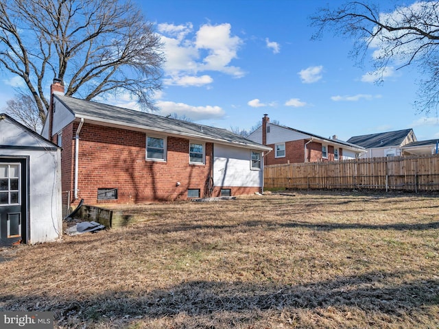 rear view of house featuring a chimney, fence, a lawn, and brick siding