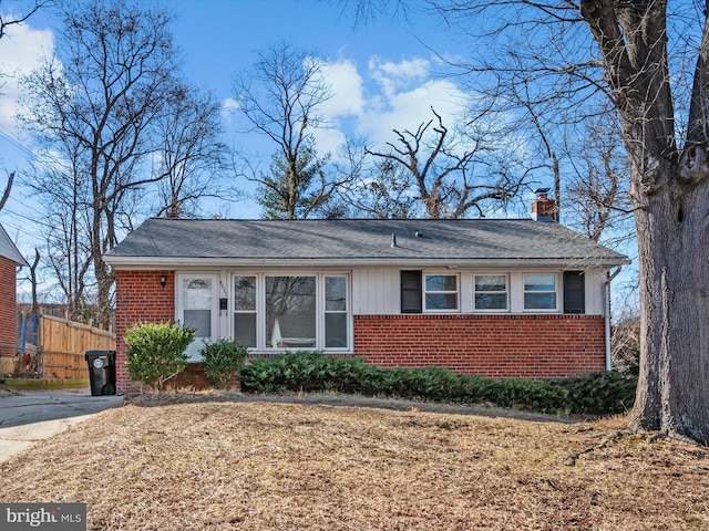 view of front facade with brick siding, a chimney, and fence