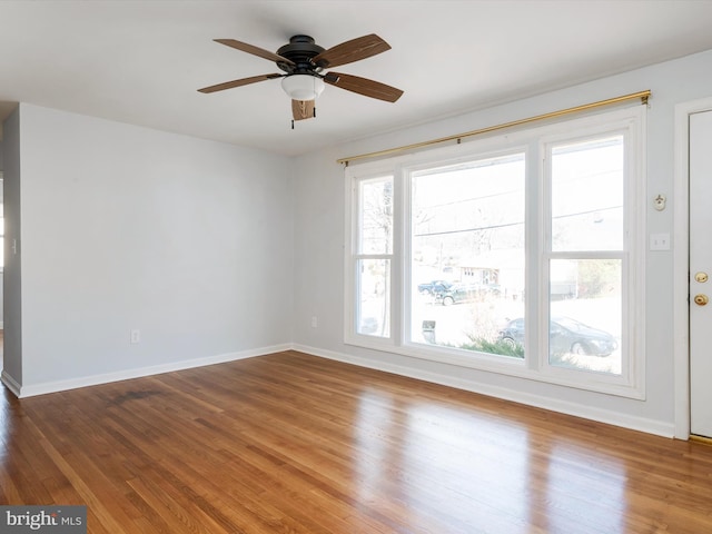 empty room with wood finished floors, a ceiling fan, and baseboards