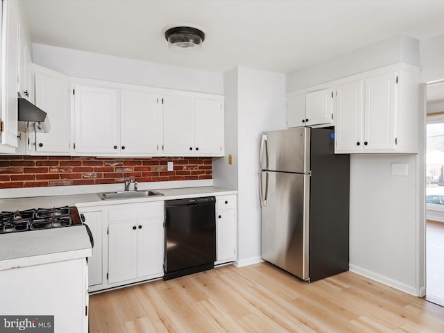 kitchen with black dishwasher, freestanding refrigerator, light countertops, white cabinetry, and a sink