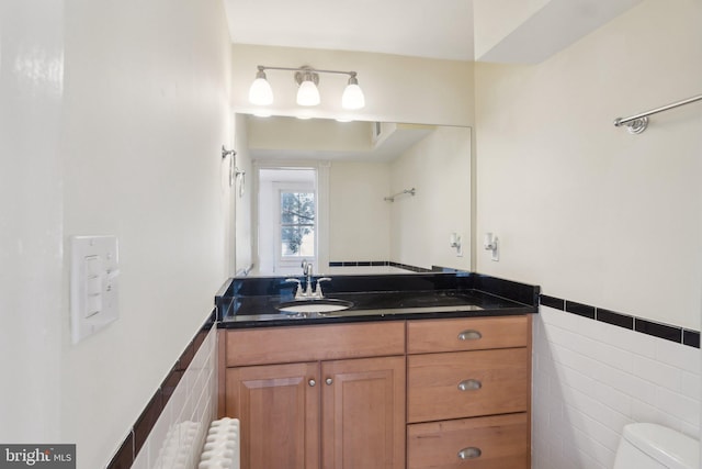 bathroom with toilet, a wainscoted wall, vanity, tile walls, and radiator