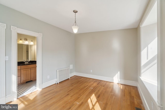 interior space featuring light wood-type flooring, baseboards, a sink, and radiator heating unit