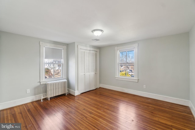 unfurnished bedroom with baseboards, visible vents, radiator heating unit, hardwood / wood-style floors, and a closet