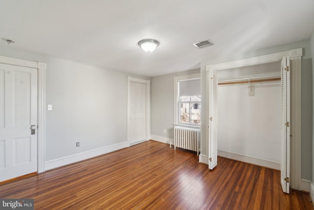 unfurnished bedroom featuring baseboards, visible vents, radiator, hardwood / wood-style floors, and a closet