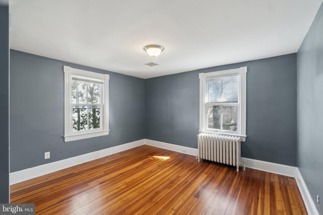 empty room featuring radiator, hardwood / wood-style flooring, visible vents, and baseboards