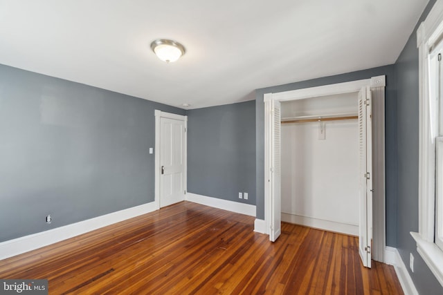 unfurnished bedroom with hardwood / wood-style floors, baseboards, and a closet