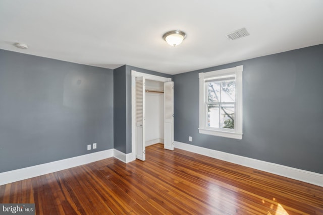 unfurnished bedroom with visible vents, a closet, baseboards, and hardwood / wood-style floors