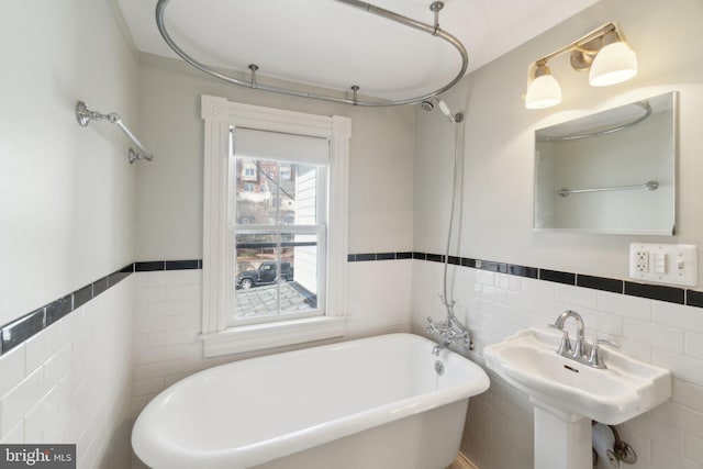 bathroom with wainscoting, a soaking tub, a sink, and tile walls