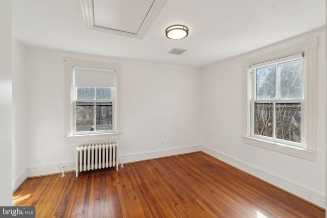 spare room with wood-type flooring, baseboards, visible vents, and radiator heating unit