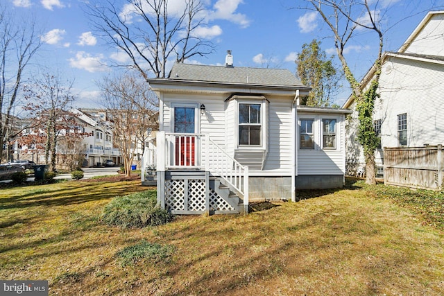 back of property with roof with shingles, a lawn, a chimney, and fence