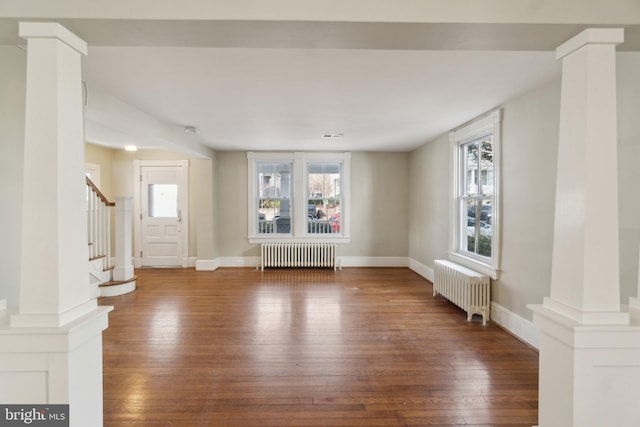 interior space featuring baseboards, radiator heating unit, hardwood / wood-style flooring, and ornate columns