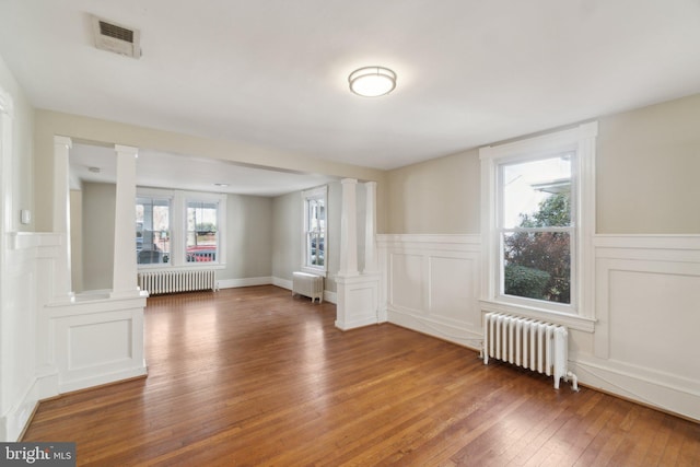 unfurnished room featuring radiator heating unit and decorative columns