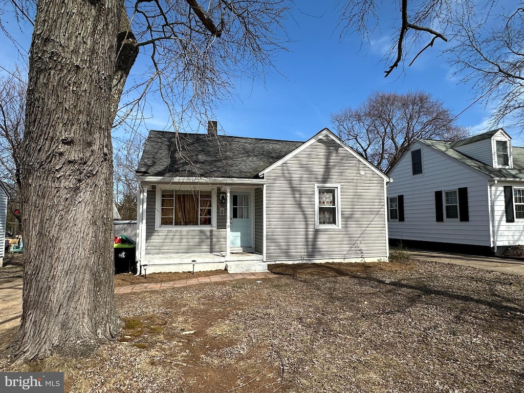 view of front facade featuring a shingled roof, a chimney, and a porch