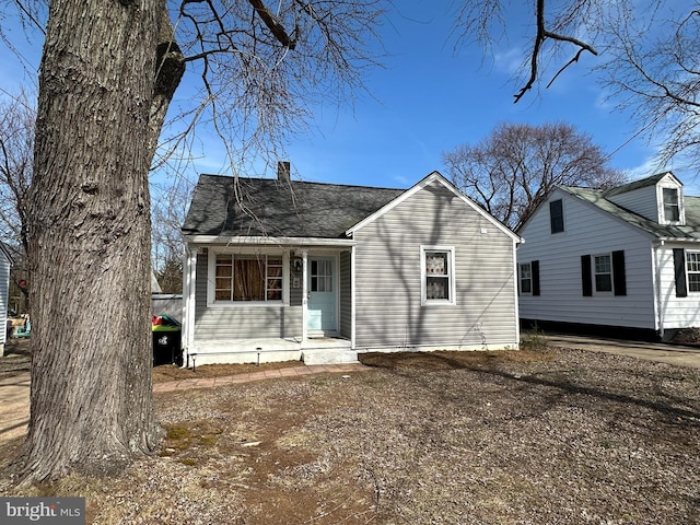 view of front facade featuring a shingled roof, a chimney, and a porch