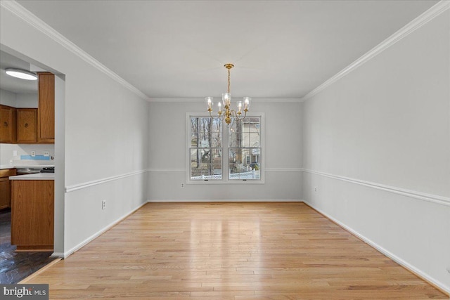 unfurnished dining area featuring light wood-type flooring, baseboards, a chandelier, and ornamental molding