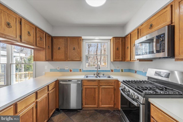 kitchen featuring appliances with stainless steel finishes, brown cabinets, light countertops, and a sink