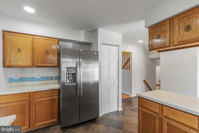 kitchen with light countertops, stone finish floor, stainless steel refrigerator with ice dispenser, and brown cabinets