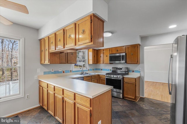 kitchen featuring light countertops, appliances with stainless steel finishes, stone finish flooring, a sink, and a peninsula