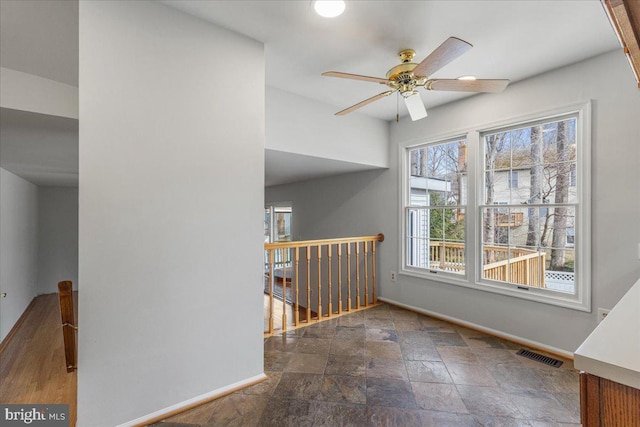 empty room featuring stone tile floors, visible vents, baseboards, and ceiling fan