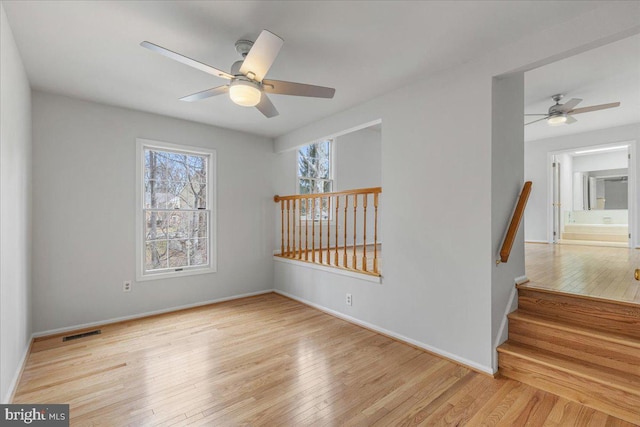 unfurnished room featuring a healthy amount of sunlight, wood-type flooring, visible vents, and baseboards