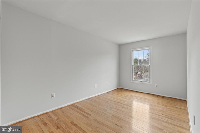 unfurnished room featuring wood-type flooring, visible vents, and baseboards