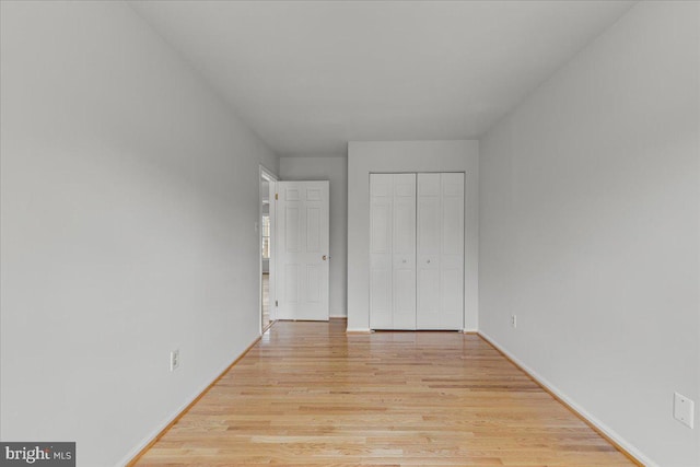 unfurnished bedroom featuring light wood-style floors, baseboards, and a closet