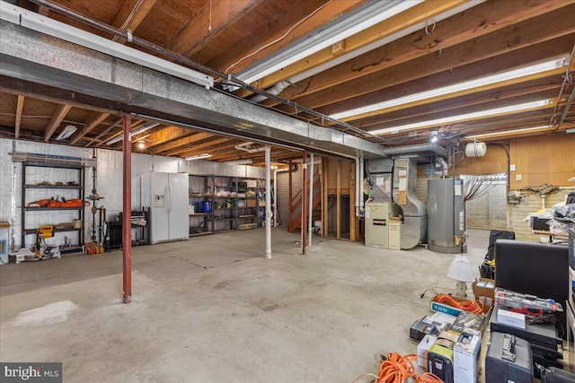 unfinished below grade area featuring water heater, white refrigerator with ice dispenser, and heating unit