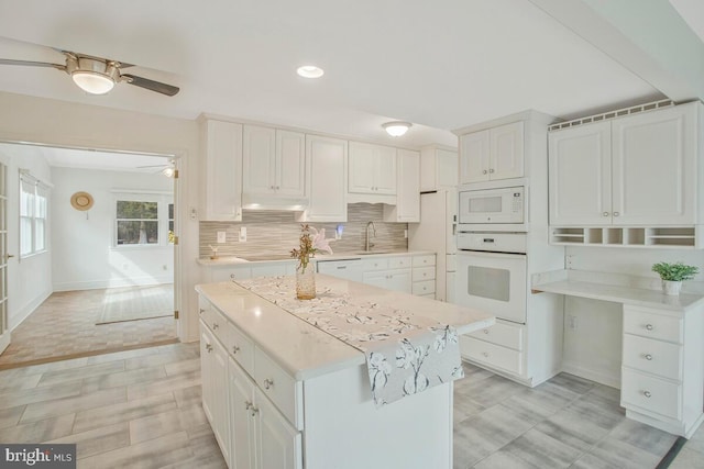 kitchen with under cabinet range hood, white appliances, a sink, light countertops, and decorative backsplash