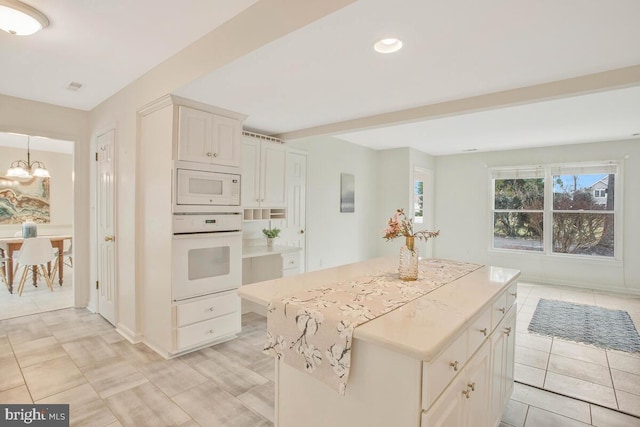 kitchen featuring white appliances, light tile patterned floors, a kitchen island, an inviting chandelier, and beam ceiling