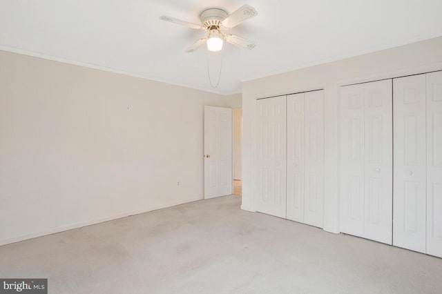 unfurnished bedroom featuring crown molding, baseboards, a ceiling fan, and multiple closets